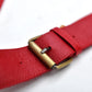 Close-up of a red leather belt with a brass buckle, showing the texture of the leather and the details of the buckle.