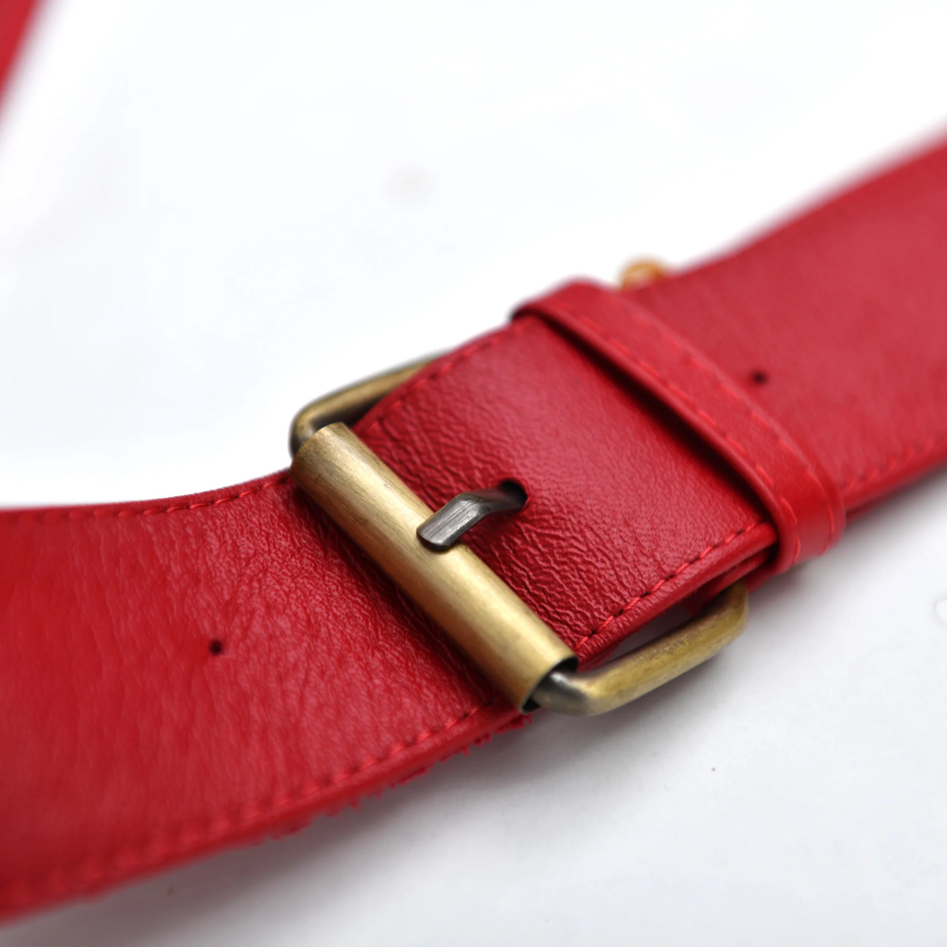 Close-up of a red leather belt with a brass buckle, showing the texture of the leather and the details of the buckle.