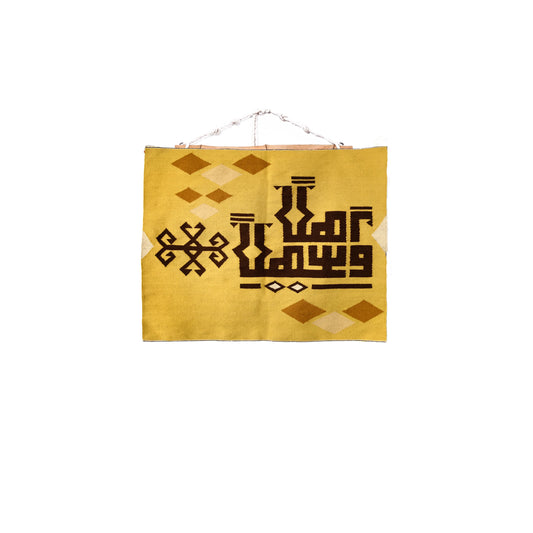 "A square woven tapestry with a yellow background featuring brown geometric patterns and Arabic calligraphy, with a hanging rod at the top."