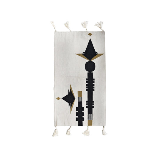 This image features a decorative textile or tapestry with an abstract design, primarily in black, gold, and cream colors. The pattern includes geometric shapes, such as triangles and vertical lines, with tassels at the bottom. The overall aesthetic is modern and artistic, likely inspired by tribal or cultural motifs.