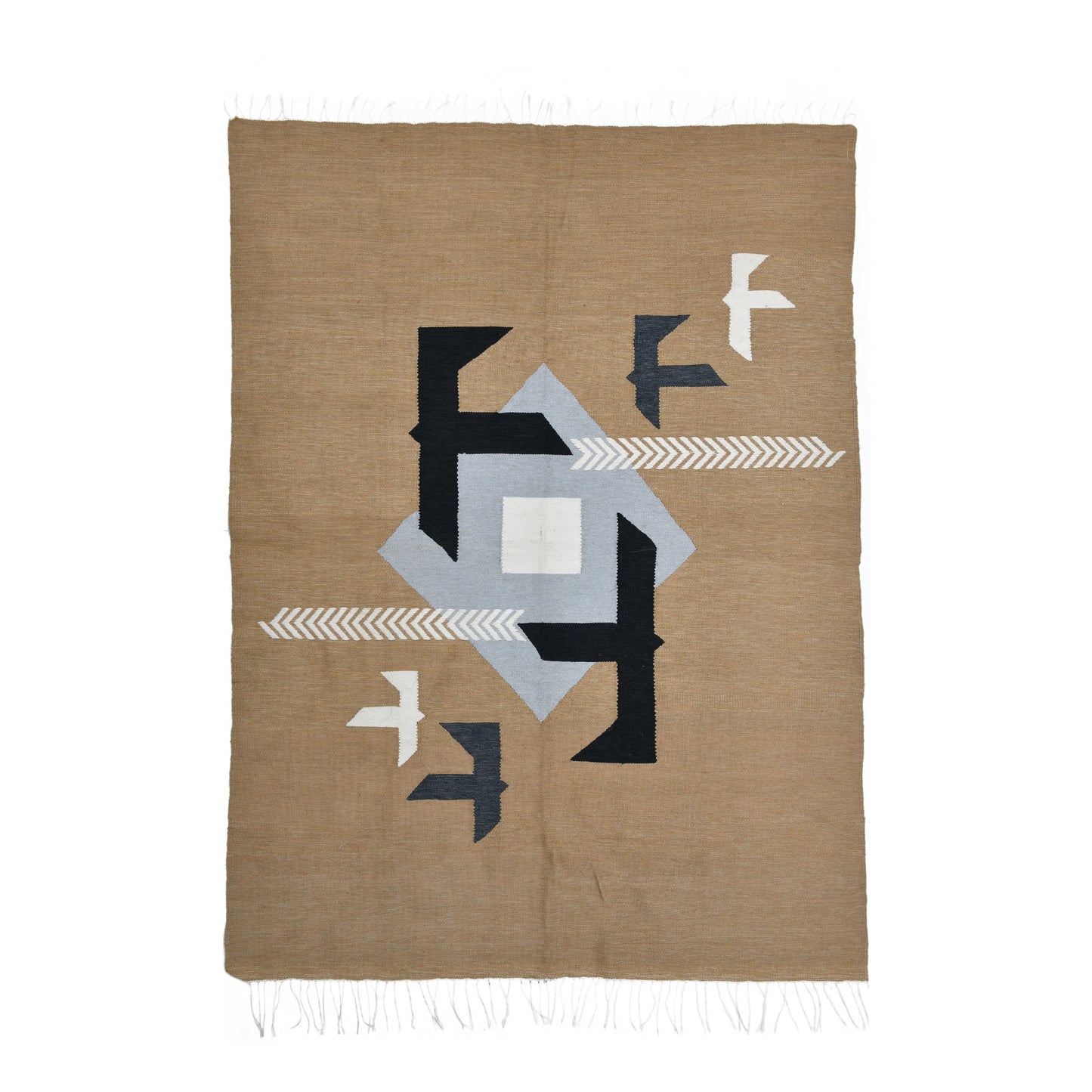 A woven textile featuring a geometric design in earthy tones. The rug is primarily beige with black, gray, and white shapes, including arrows and stylized birds. The edges of the rug are finished with fringes, adding a decorative touch.