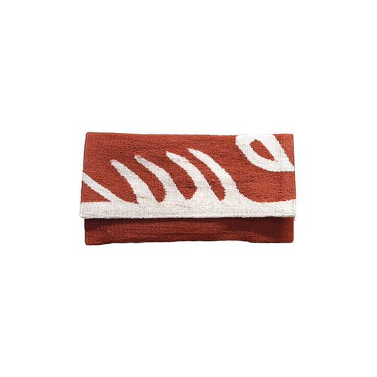 "A flat woven clutch in terracotta with bold abstract white leaf patterns. The clutch is neatly folded, showcasing its textured fabric and modern design."