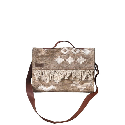 A woven handbag is presented against a white background. The bag features a warm beige color with white geometric patterns and fringed detailing at the bottom. It has a brown leather strap, adding an elegant touch to its design. The overall appearance is both stylish and functional, highlighting the craftsmanship of the bag.