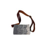 "A gray woven crossbody bag with a textured pattern, featuring a brown leather strap. The bag is laid flat against a white background, showcasing its design and craftsmanship."