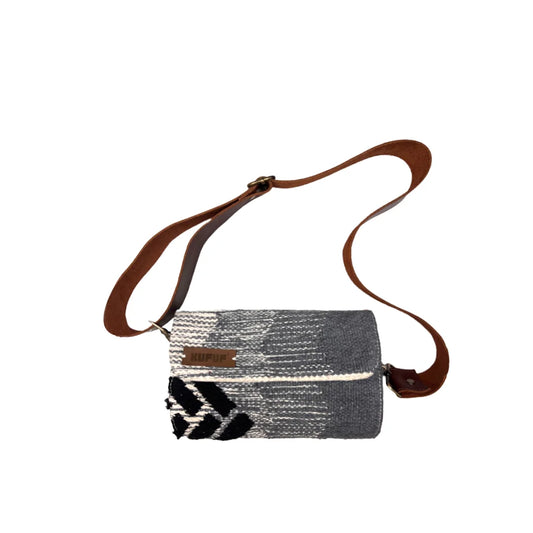 "A gray and white woven bag with a patterned design, featuring a distinct black geometric element and a brown leather strap. The bag is positioned against a white background."