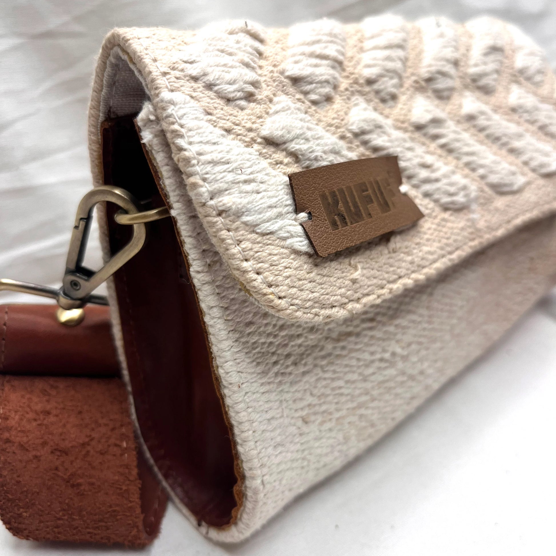  "A side view of a cream-colored woven bag showcasing its white chevron pattern and a leather tag that reads 'KUFUF.' The image captures the bag's clasp and detailing."